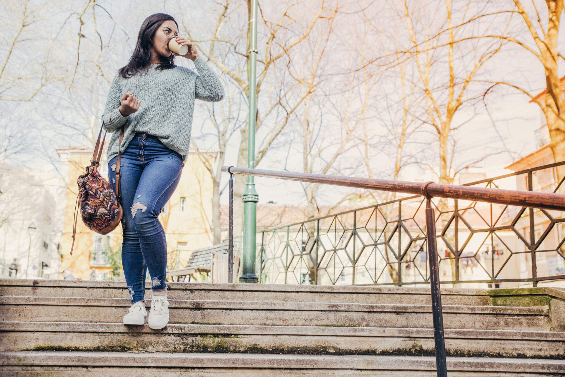 Young woman in ripped jeans drinking a coffee and walking down some city steps Young woman in ripped jeans drinking a coffee and walking down some city steps